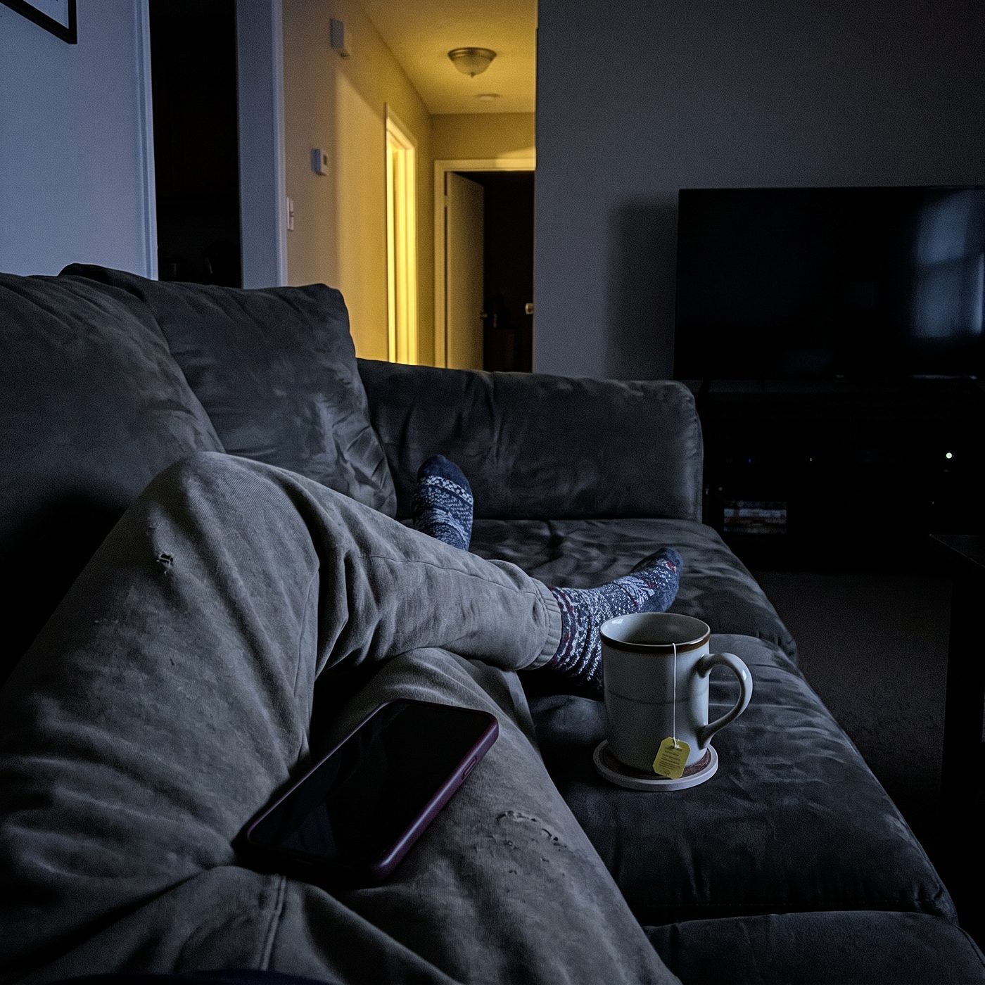A parent alone on the couch late at night, cold tea, phone face-down
